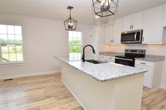 kitchen featuring sink, white cabinets, stainless steel appliances, a center island with sink, and light stone countertops