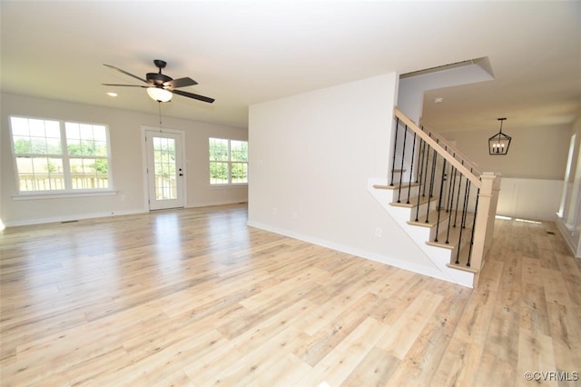 unfurnished living room with ceiling fan with notable chandelier and light wood-type flooring