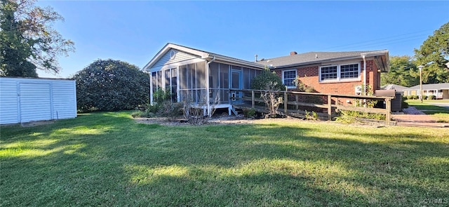 rear view of house with a sunroom, a yard, and a storage unit