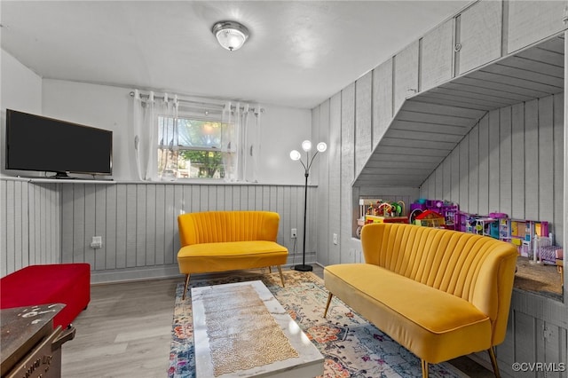 living area with lofted ceiling, light hardwood / wood-style flooring, and wooden walls