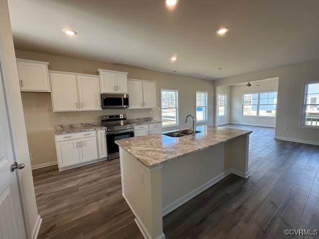 kitchen featuring stainless steel appliances, light stone countertops, an island with sink, white cabinets, and dark hardwood / wood-style flooring