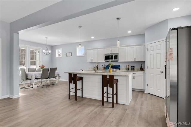 kitchen with pendant lighting, a kitchen bar, a center island with sink, white cabinets, and appliances with stainless steel finishes