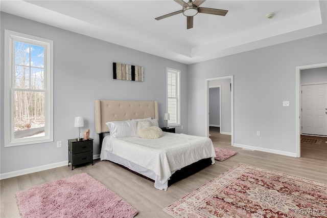 bedroom featuring ceiling fan, light hardwood / wood-style flooring, and a tray ceiling