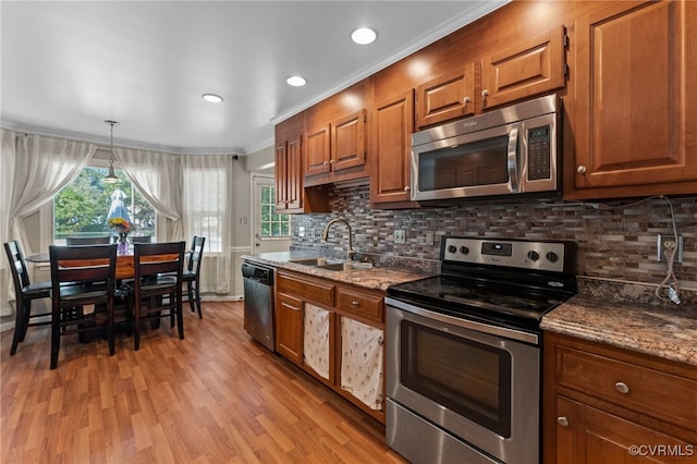 kitchen with appliances with stainless steel finishes, stone counters, ornamental molding, and light hardwood / wood-style flooring