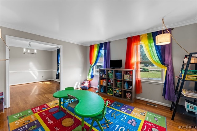 recreation room featuring wood-type flooring, ornamental molding, and an inviting chandelier