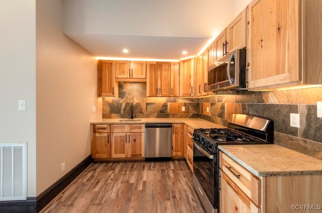 kitchen featuring light brown cabinets, hardwood / wood-style floors, appliances with stainless steel finishes, and tasteful backsplash