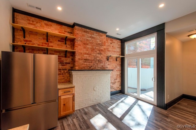 kitchen with ornamental molding, dark wood-type flooring, brick wall, and stainless steel refrigerator