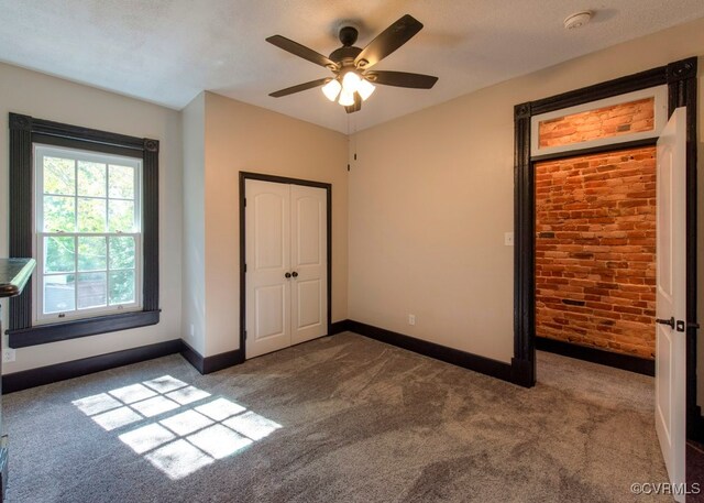 unfurnished bedroom featuring dark colored carpet, brick wall, ceiling fan, a textured ceiling, and a closet