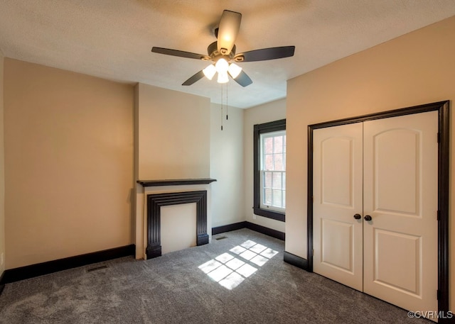 unfurnished living room with ceiling fan, a textured ceiling, and dark carpet