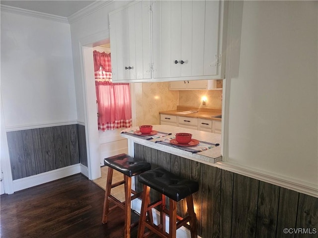 kitchen with white cabinetry, dark wood-type flooring, ornamental molding, and a breakfast bar