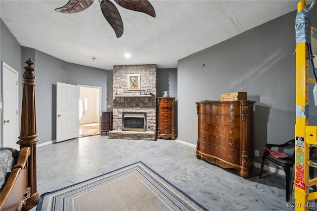 living room featuring ceiling fan, a stone fireplace, a textured ceiling, and concrete flooring