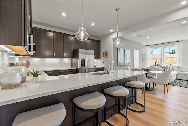 kitchen featuring stainless steel fridge, light hardwood / wood-style flooring, a kitchen breakfast bar, sink, and hanging light fixtures