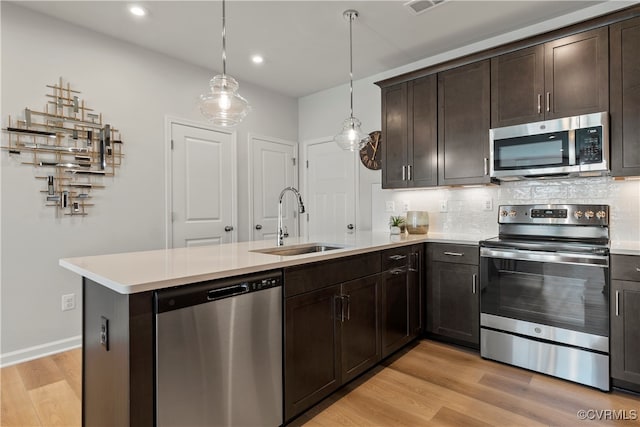 kitchen with hanging light fixtures, sink, dark brown cabinets, stainless steel appliances, and light wood-type flooring