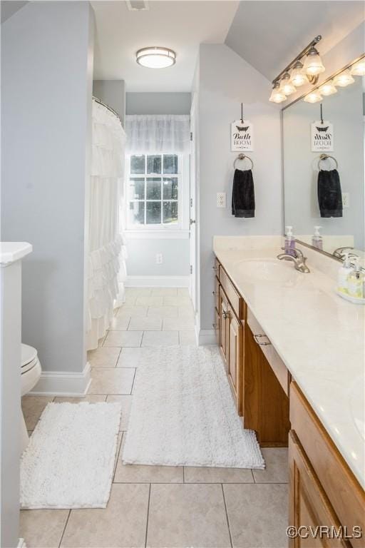 bathroom with toilet, vaulted ceiling, vanity, baseboards, and tile patterned floors