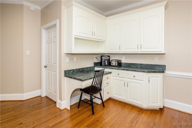 kitchen featuring dark countertops, light wood-type flooring, white cabinets, and built in desk