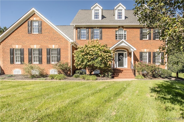 colonial house featuring a shingled roof, brick siding, and a front lawn