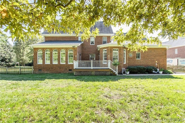 rear view of property featuring brick siding, fence, a deck, and a lawn