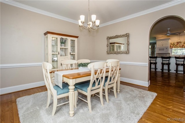 dining space with baseboards, arched walkways, wood finished floors, crown molding, and a notable chandelier