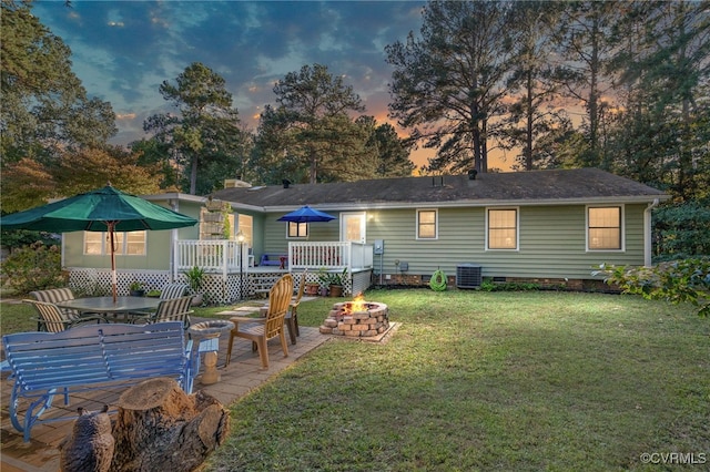 back house at dusk featuring central AC, a yard, a fire pit, and a wooden deck