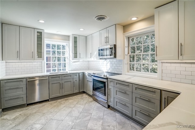 kitchen with a healthy amount of sunlight, backsplash, stainless steel appliances, and gray cabinets