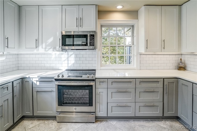 kitchen with white cabinets, stainless steel appliances, backsplash, and gray cabinetry