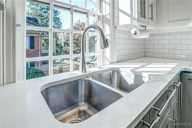 room details with white cabinetry, backsplash, sink, and light stone counters