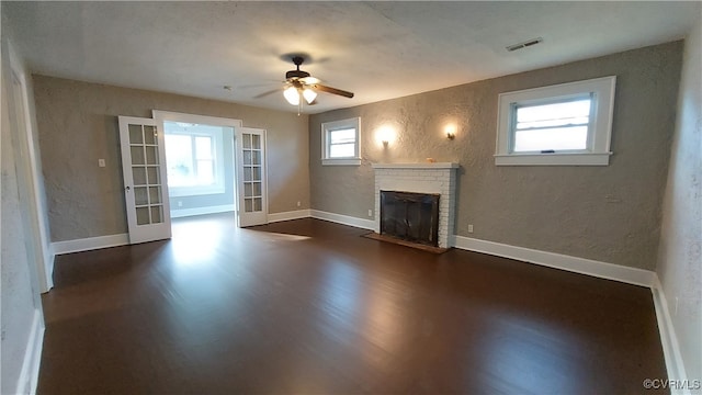 unfurnished living room with french doors, a brick fireplace, ceiling fan, and dark wood-type flooring