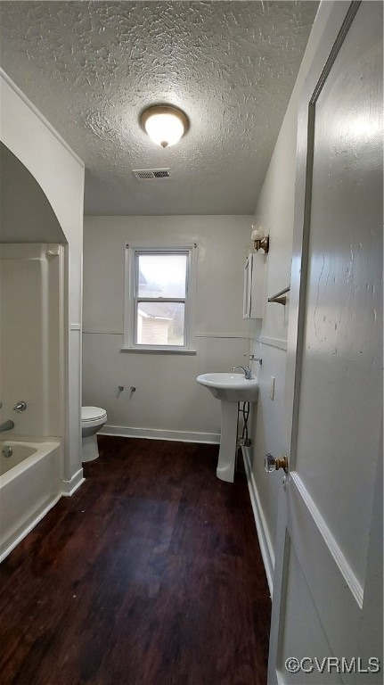 full bathroom with bathing tub / shower combination, a textured ceiling, hardwood / wood-style flooring, and toilet