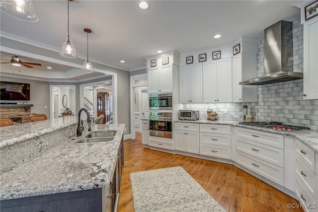 kitchen featuring sink, pendant lighting, wall chimney range hood, appliances with stainless steel finishes, and a center island with sink