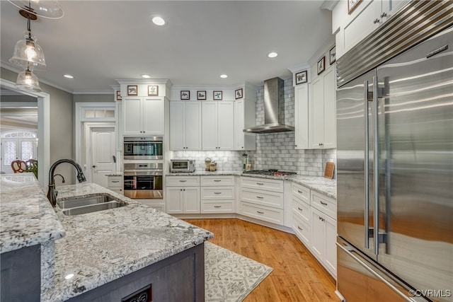 kitchen with wall chimney exhaust hood, sink, hanging light fixtures, appliances with stainless steel finishes, and ornamental molding