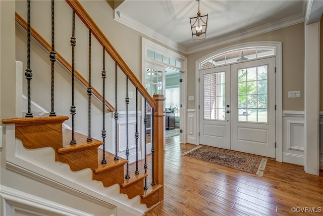 foyer entrance with crown molding, a chandelier, french doors, and light hardwood / wood-style floors