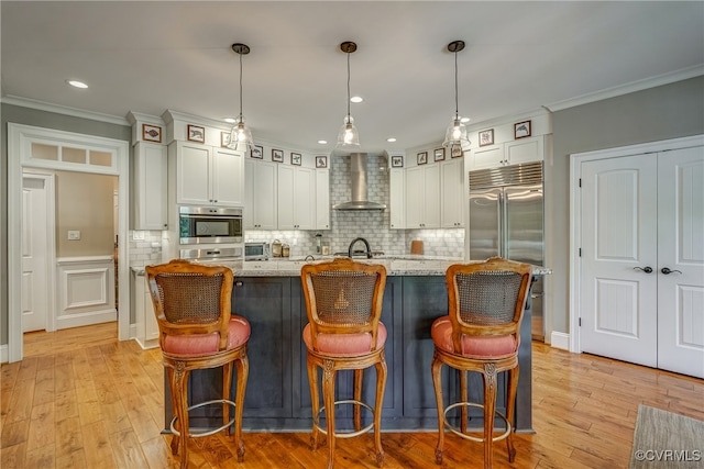 kitchen with appliances with stainless steel finishes, pendant lighting, light stone counters, and wall chimney range hood