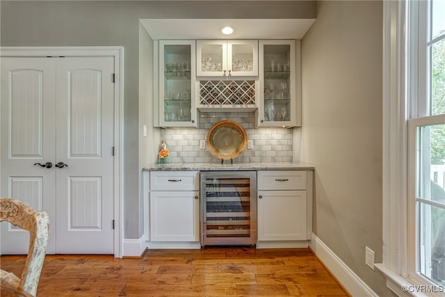 bar with beverage cooler, light hardwood / wood-style flooring, and a healthy amount of sunlight