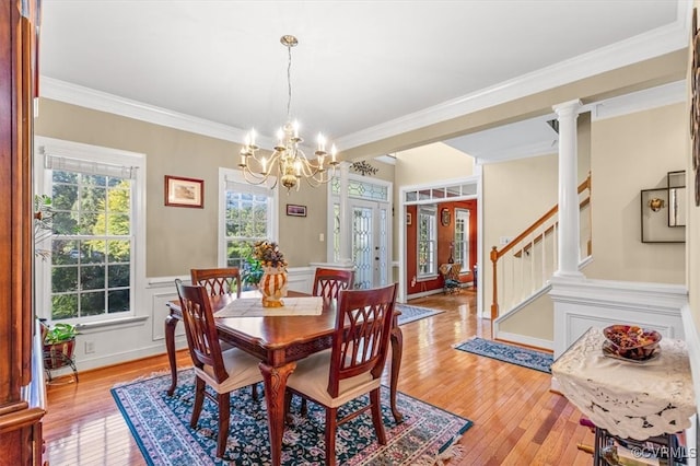 dining room featuring a notable chandelier, light wood-type flooring, ornamental molding, and decorative columns