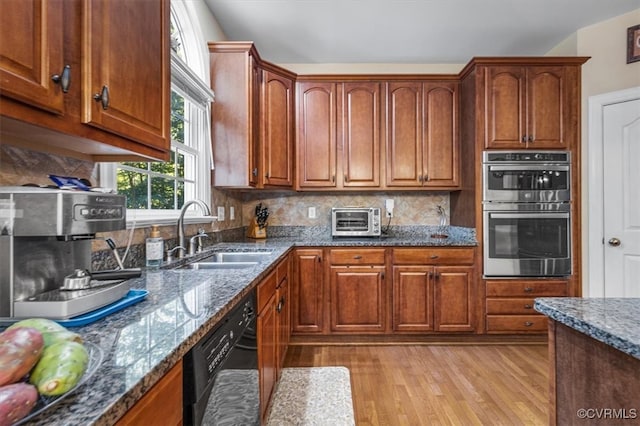 kitchen featuring sink, dark stone countertops, black dishwasher, light hardwood / wood-style floors, and stainless steel double oven