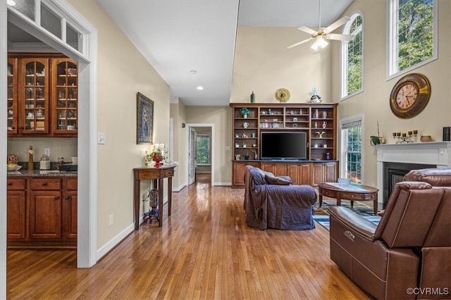 living room with ceiling fan, light wood-type flooring, and a towering ceiling