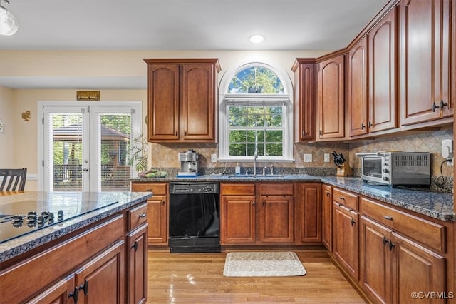 kitchen featuring black appliances, sink, decorative backsplash, dark stone countertops, and light wood-type flooring