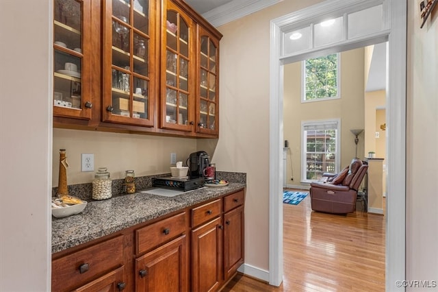 bar featuring dark stone countertops, light hardwood / wood-style flooring, and ornamental molding