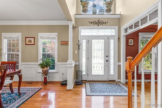 foyer entrance featuring decorative columns, ornamental molding, and light wood-type flooring