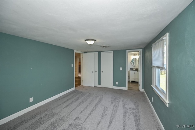 unfurnished bedroom featuring light colored carpet, ensuite bathroom, and a textured ceiling