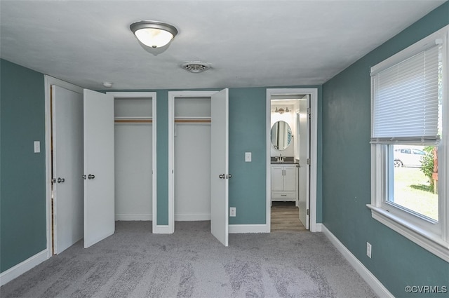 unfurnished bedroom featuring ensuite bath, two closets, and light colored carpet