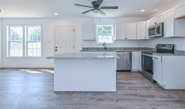 kitchen with light hardwood / wood-style flooring, white cabinetry, appliances with stainless steel finishes, a center island, and light stone countertops