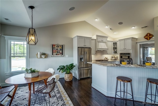 kitchen featuring pendant lighting, dark wood-type flooring, stainless steel appliances, custom range hood, and vaulted ceiling