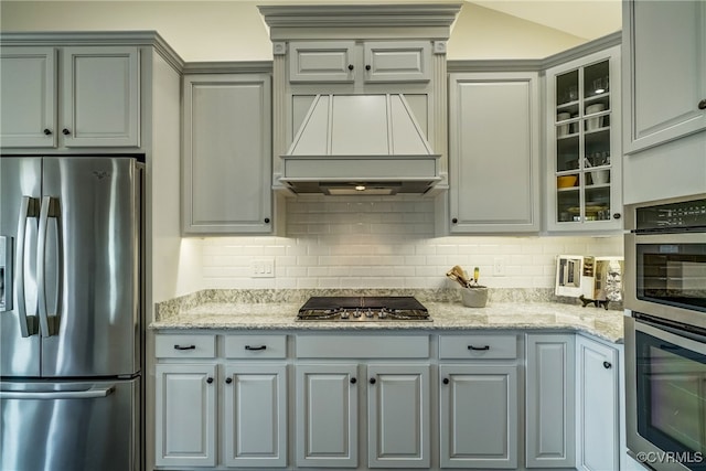 kitchen with light stone counters, stainless steel appliances, backsplash, and gray cabinetry