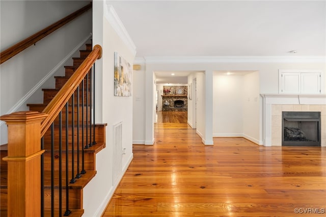 interior space featuring wood-type flooring, crown molding, and a tile fireplace