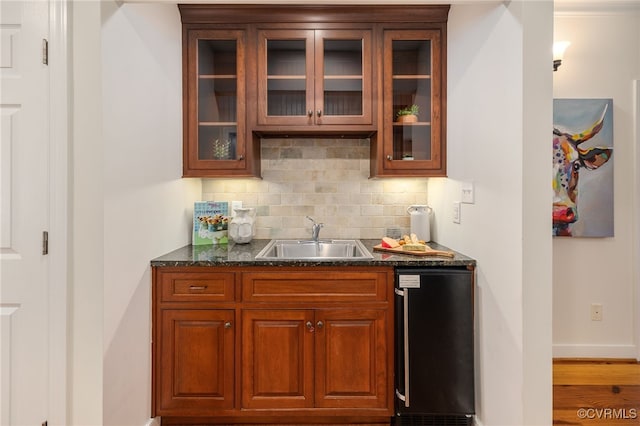 bar with wood-type flooring, sink, dark stone counters, black dishwasher, and backsplash