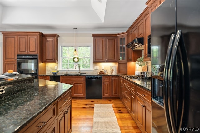 kitchen with pendant lighting, light hardwood / wood-style flooring, dark stone countertops, sink, and black appliances