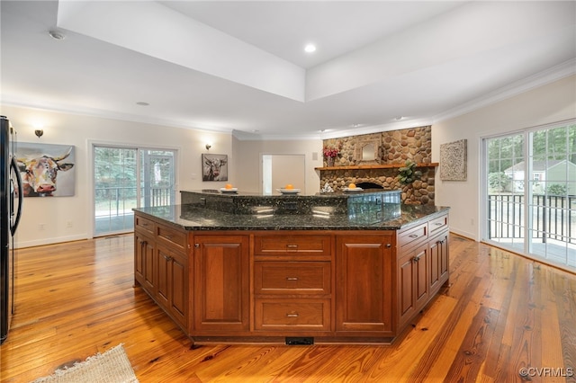 kitchen featuring dark stone countertops, plenty of natural light, a stone fireplace, and light hardwood / wood-style flooring