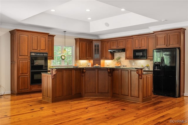 kitchen featuring a raised ceiling, dark stone counters, black appliances, and light wood-type flooring