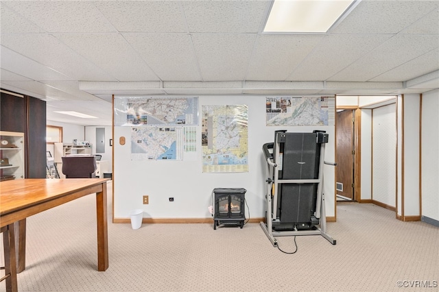 exercise room with a drop ceiling, a wood stove, and light carpet